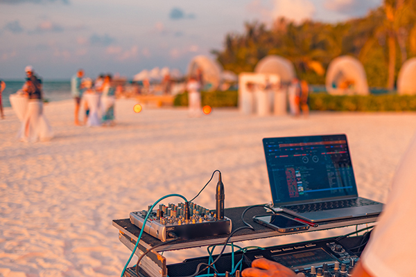 DJ performing at outdoor beach party at sunset with crowd dancing by the sea